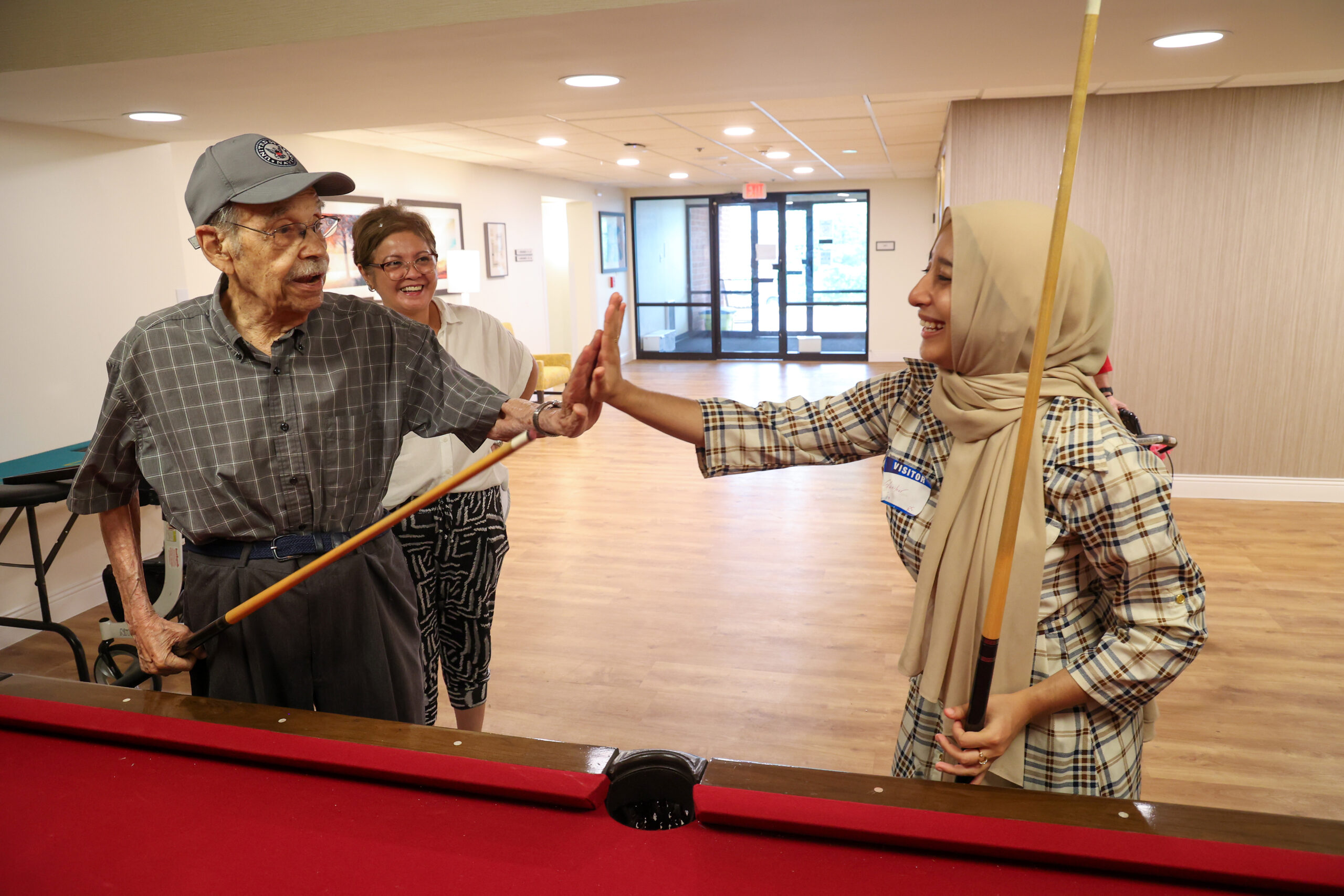 A teen and an elderly man hi five while holding pool sticks after playing a game of pool