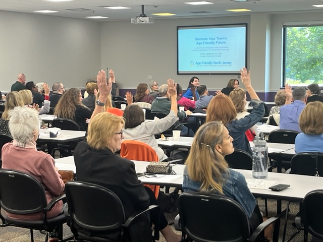 A crowd sits at multiple tables, some raising their hands