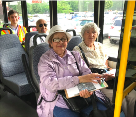 Two elderly women, an older man, and a young adult sit on a bus looking at the camera