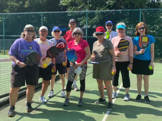 A group of people stand on a pickleball court with paddles and balls