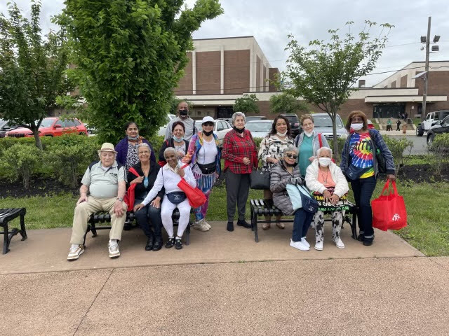 A multi-ethnic group of seniors pose for a group picture while sitting on park benches